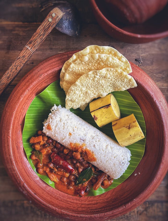 A delicious Sri Lankan breakfast featuring puttu, curry, banana, and poppadoms on a banana leaf.